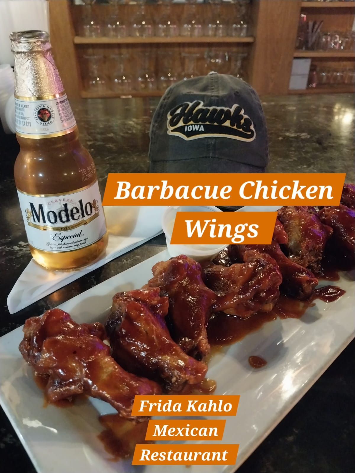 A plate of barbecue chicken wings next to a bottle of modelo beer