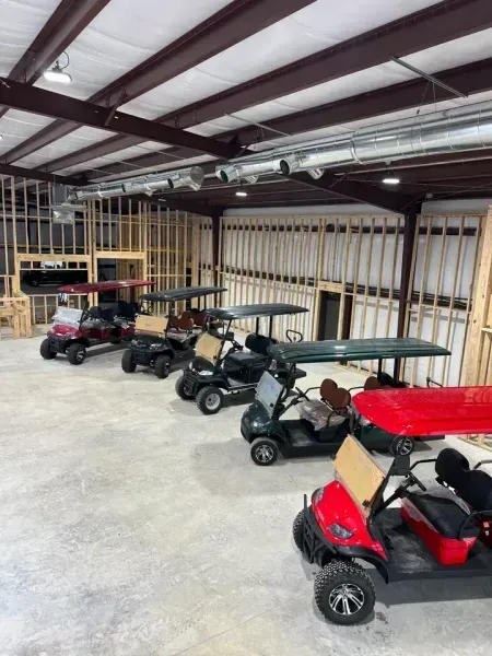 A fleet of four golf carts in red, black, and green parked in a spacious, unfinished industrial warehouse space.