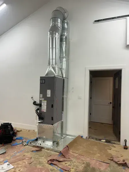 A gray HVAC unit with vertical metal ductwork installed against a white wall next to an open doorway.