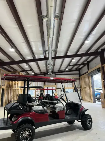 A red golf cart parked inside a large, open metal-frame building under construction with exposed rafters and HVAC ducts.