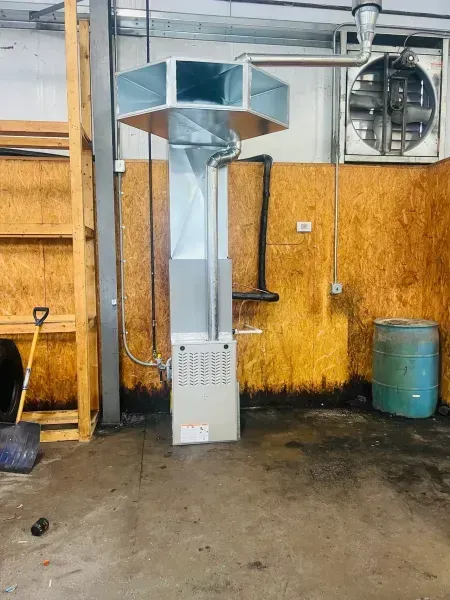 A metal HVAC unit with a large duct manifold attached, situated in a utility space with wooden walls and a blue barrel.
