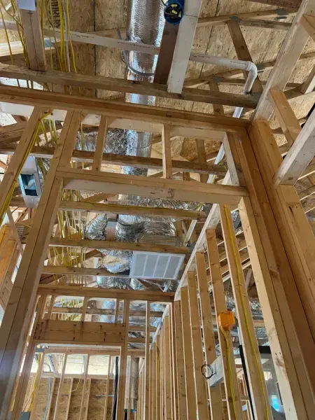 A low-angle view of interior wooden wall framing under construction, featuring exposed rafters, ductwork, and wiring.