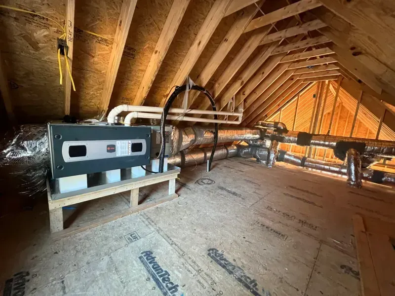 An HVAC unit sits on a wooden stand in an unfinished attic with exposed rafters and ductwork.