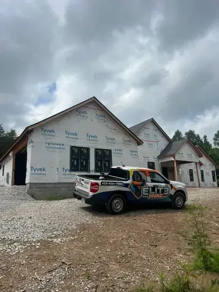 An Elite HVAC truck parked in front of a house under construction with white Tyvek house wrap against a cloudy sky.