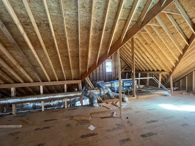 An unfinished attic space with wooden roof framing, exposed OSB flooring, and central HVAC ductwork.