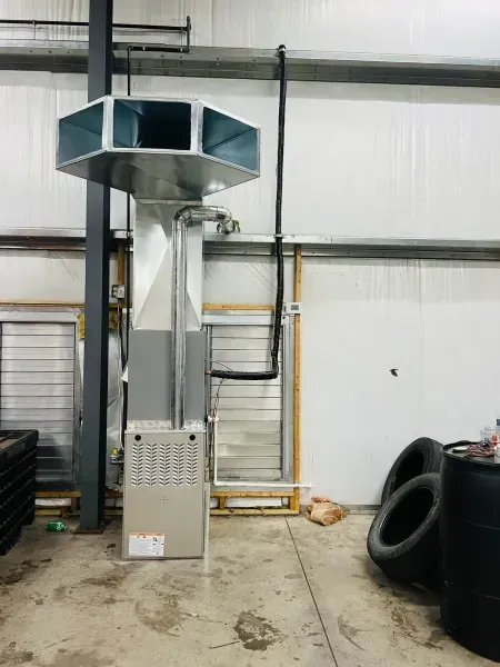 A metal HVAC furnace unit with a multi-directional duct manifold stands in an industrial warehouse space.