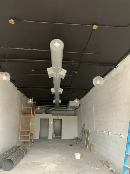 An interior construction site with white walls, a black ceiling, exposed ductwork, and hanging globe light fixtures.