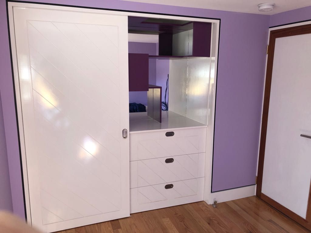 A bedroom with purple walls and white cabinets