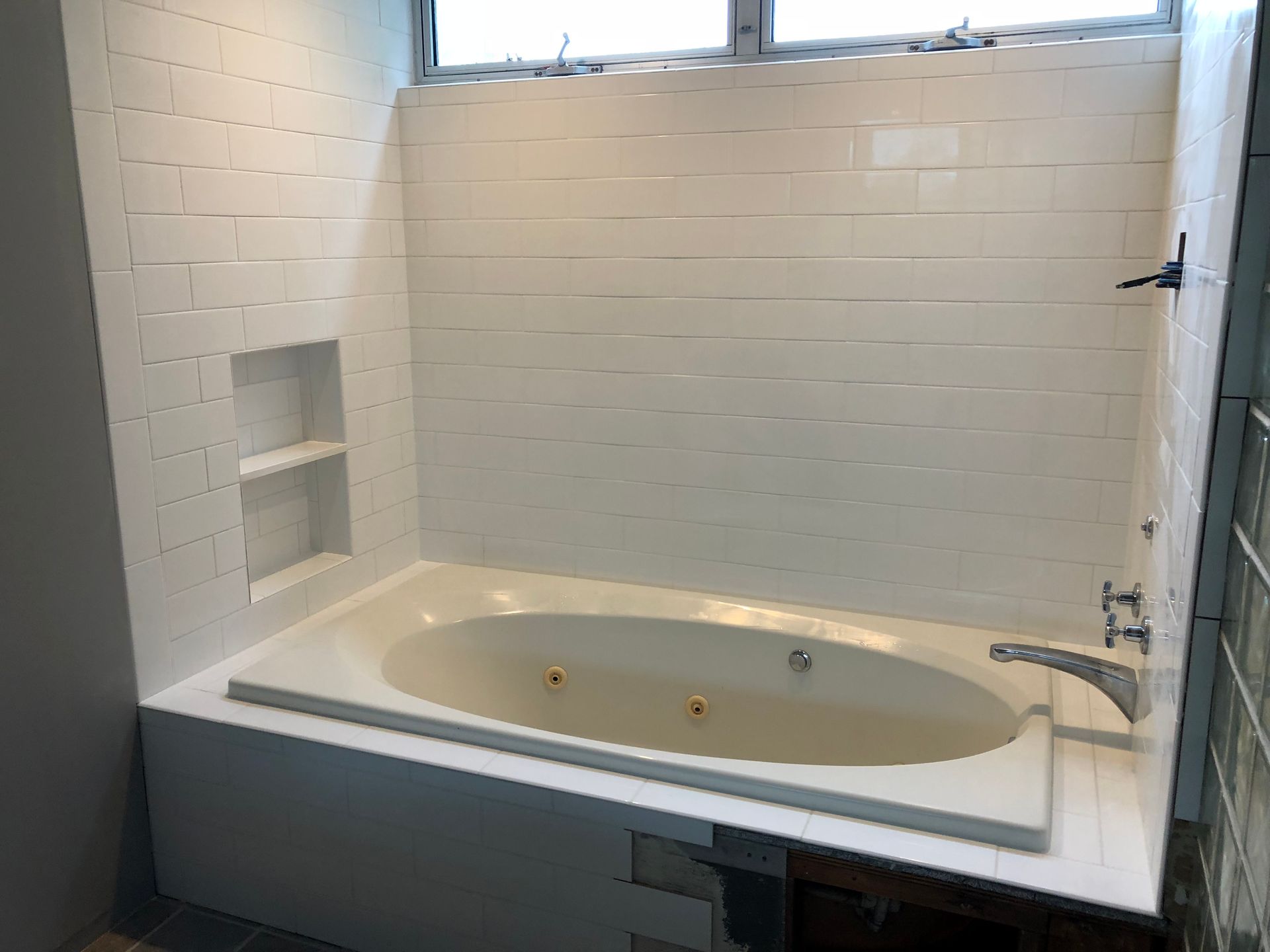 A bathtub in a bathroom with white tiles and a window.