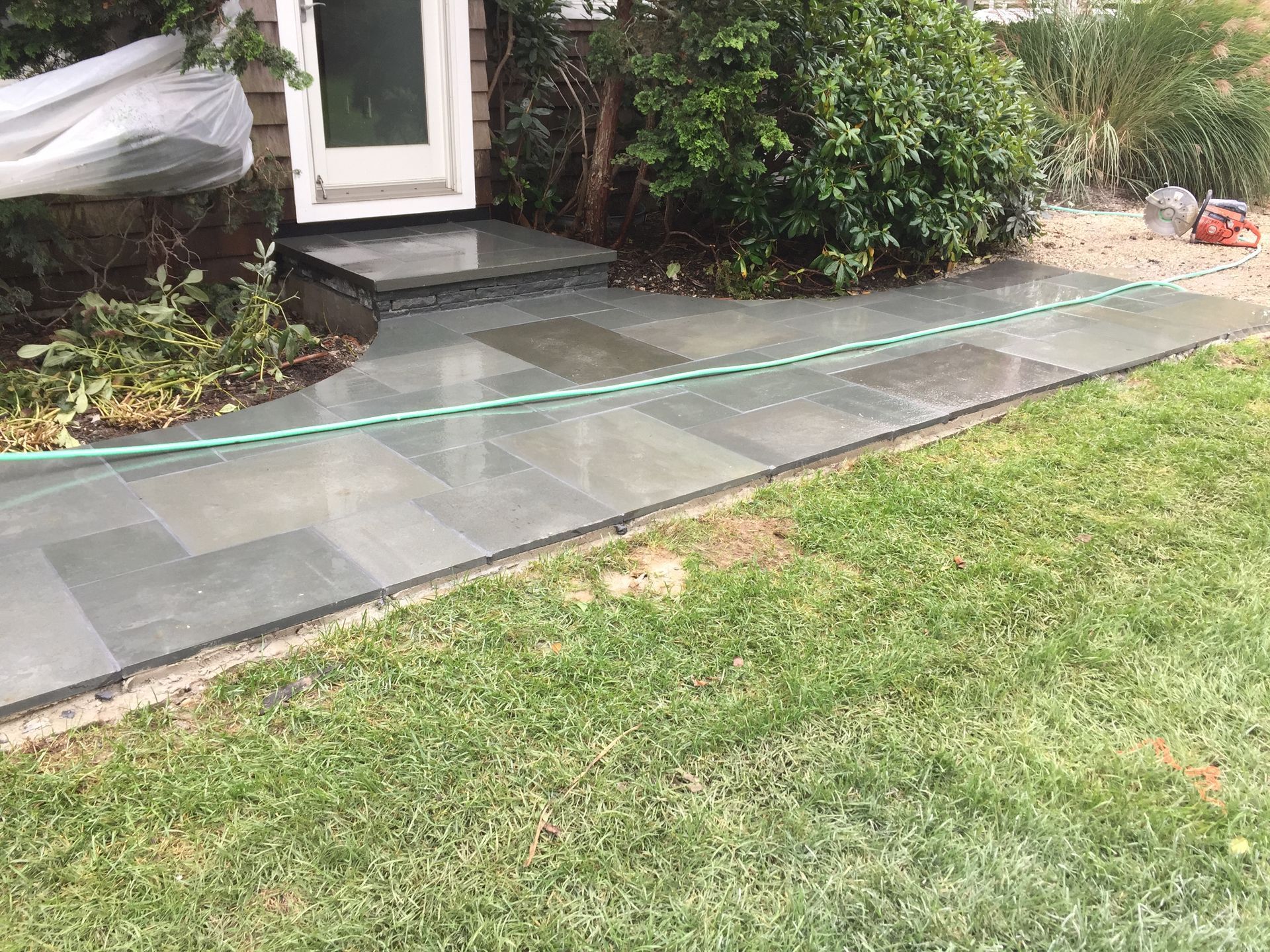 A hose is laying on the sidewalk in front of a house.