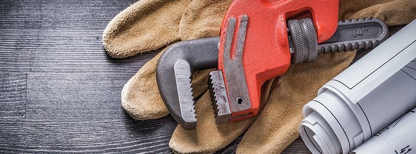 Gloves, wrench, and blueprints on a gray wooden surface, suggesting plumbing or construction.