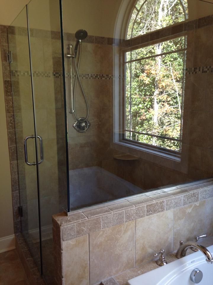 A modern shower enclosure with a window, tan tiles, and a bathtub.