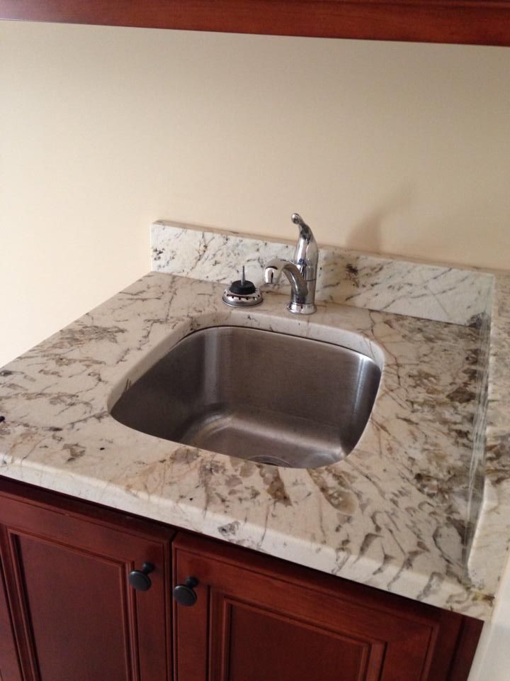 Stainless steel sink in a granite countertop set into a dark wood cabinet.