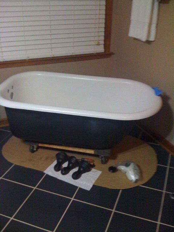 Black and white clawfoot bathtub on a brown mat, with faucet parts on the floor.