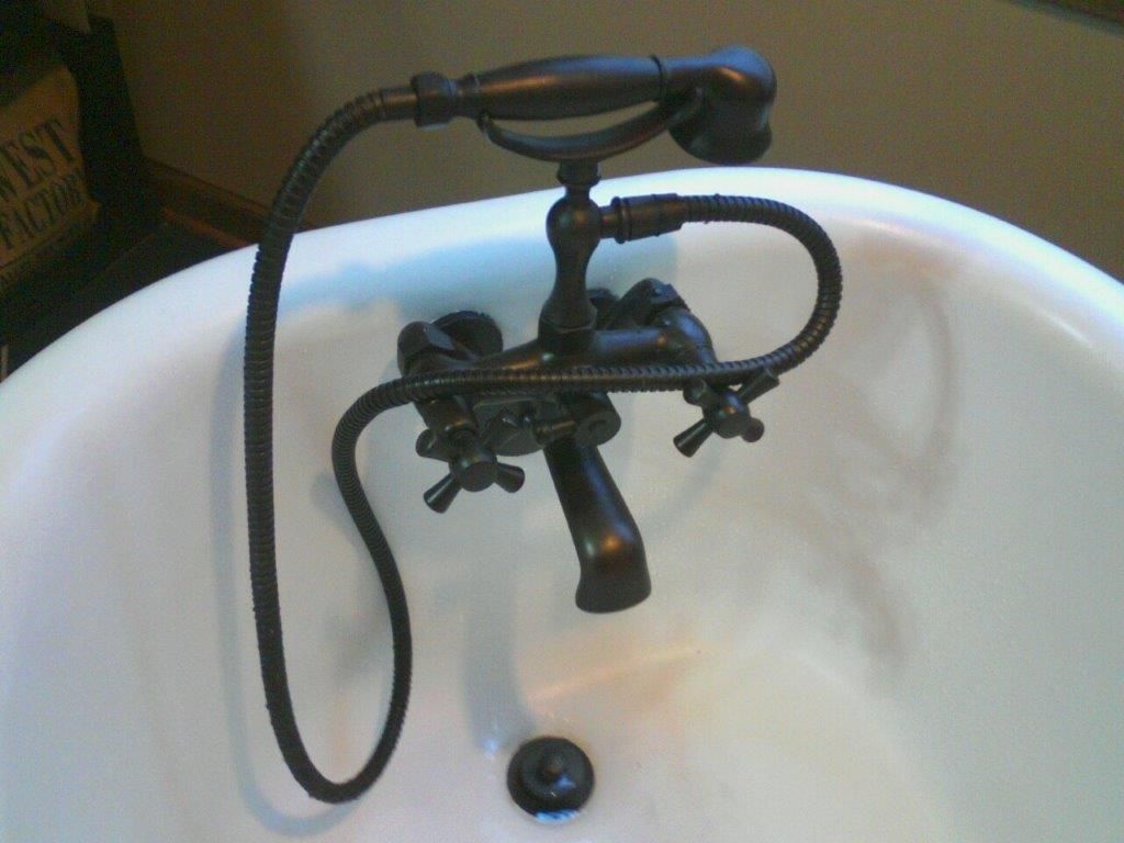 Bronze faucet and handheld shower over a white bathtub.