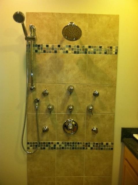 Shower with multiple showerheads and jets on beige tiled wall.