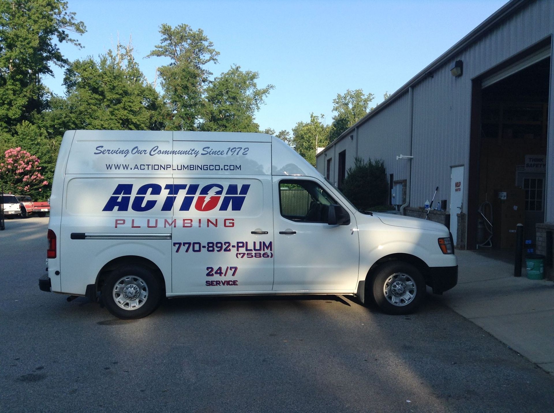 White Action Plumbing van parked outside a building with trees in the background.