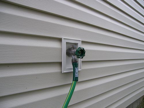 Green garden hose connected to a faucet on a white vinyl-sided house.