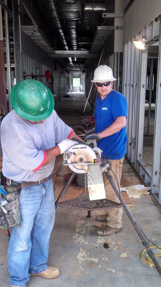 Two construction workers in a building, one using a circular saw. Inside a building under construction.