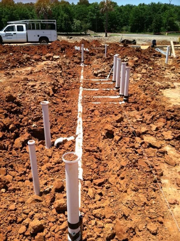 Construction site with white PVC pipes in trenches, dirt, and a work truck.