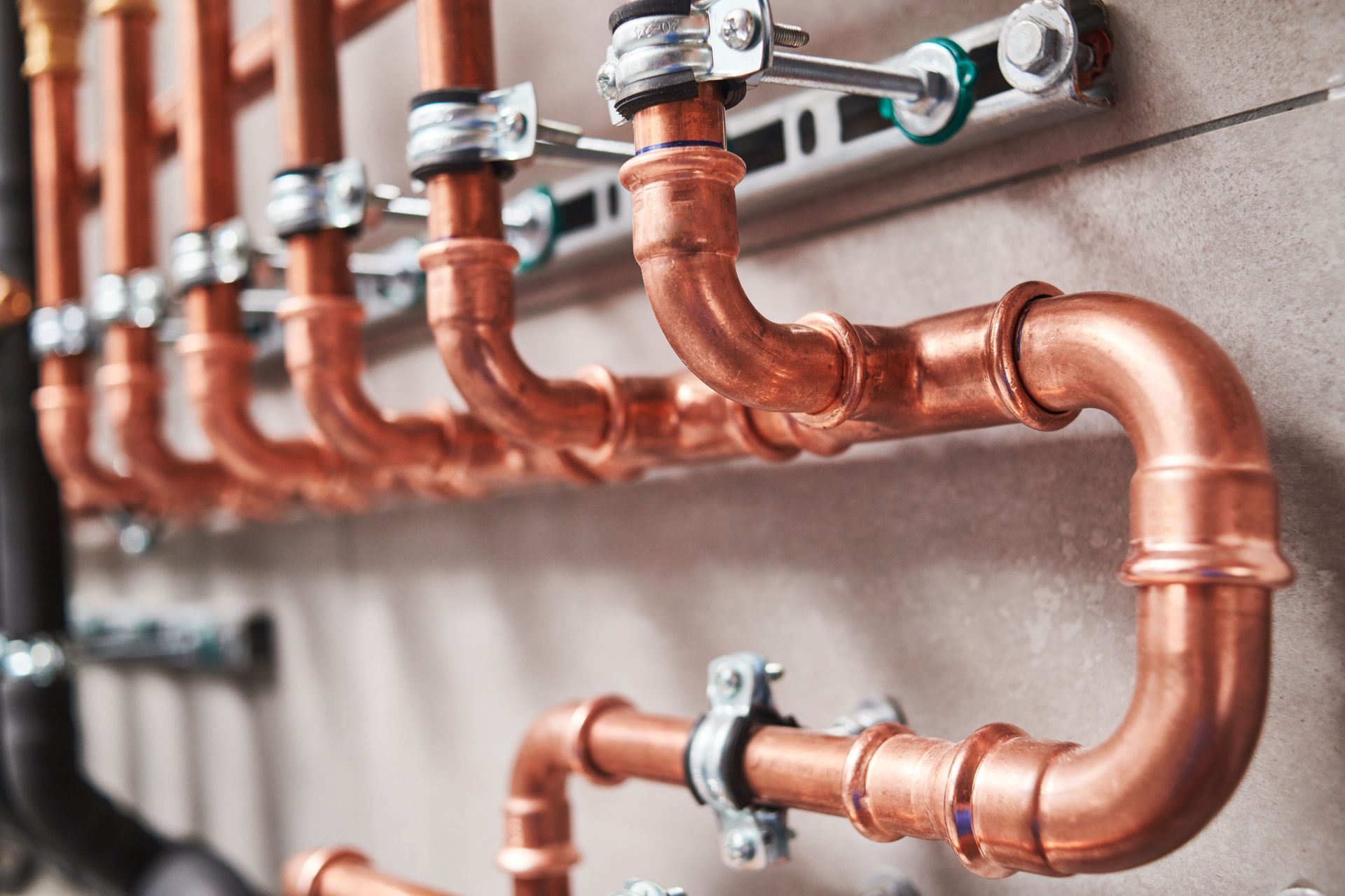 Copper pipes mounted on a light-colored wall, with silver brackets and a few black pipes in the background.