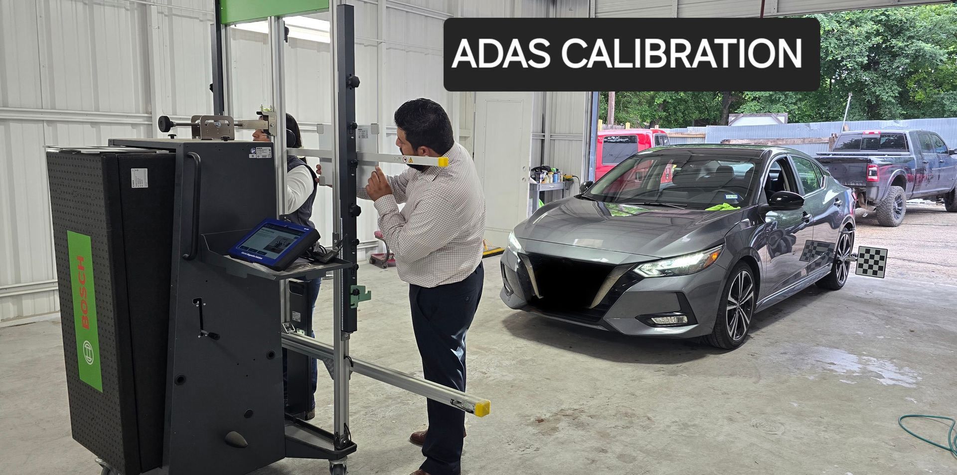 A person calibrates a car's ADAS system in a workshop. A gray car faces the equipment.