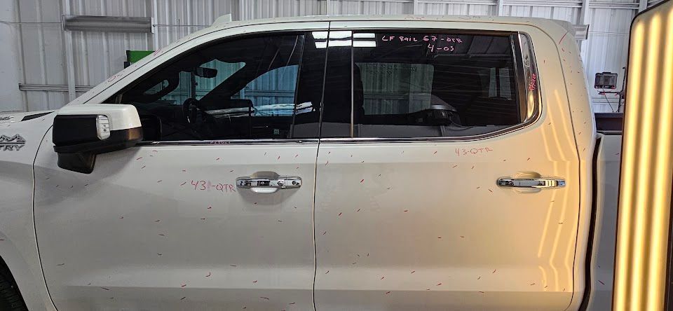 White pickup truck in a shop, with dents in the side panels, and light reflection.