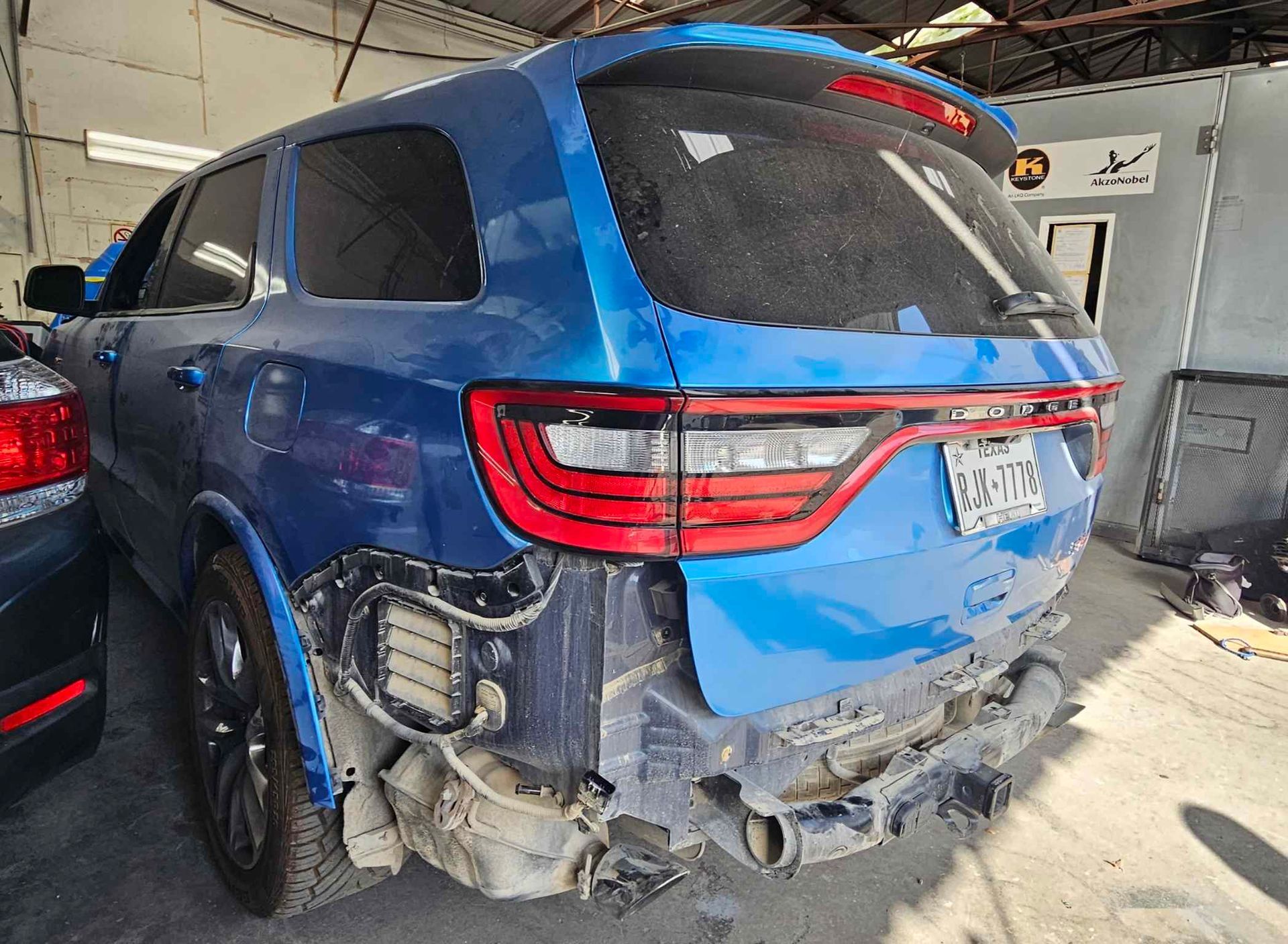 Blue SUV with rear bumper damage in a repair shop.