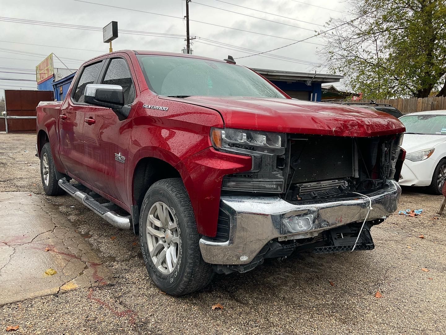 Red pickup truck with front-end damage parked outside a building on an overcast day.