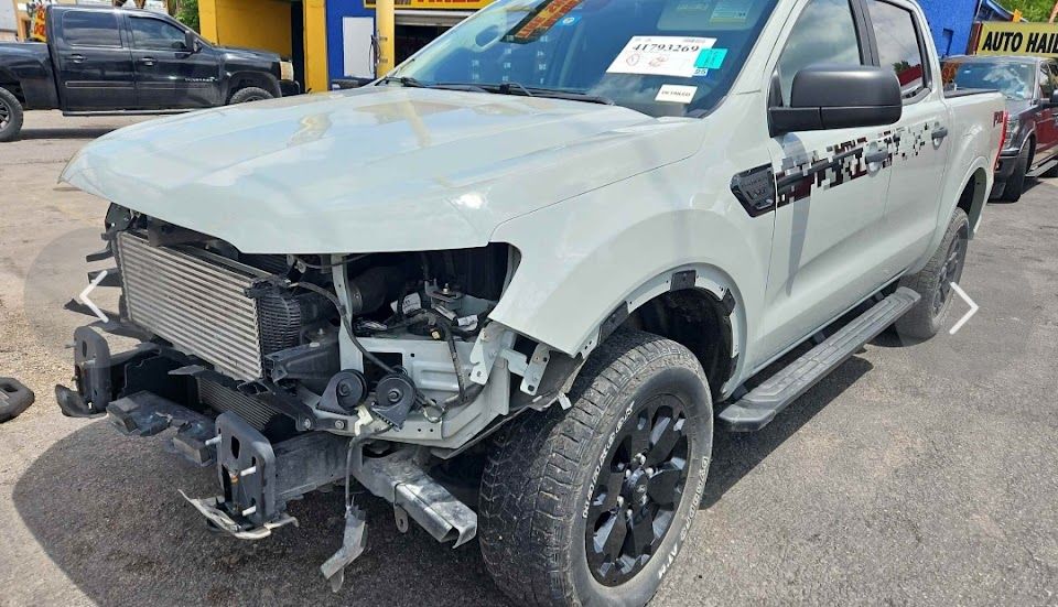 Damaged light gray Ford Ranger pickup truck in a salvage yard. Front end heavily damaged.