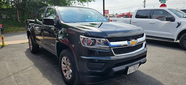 Black Chevrolet Colorado pickup truck parked in front of a white truck, likely a Ford.
