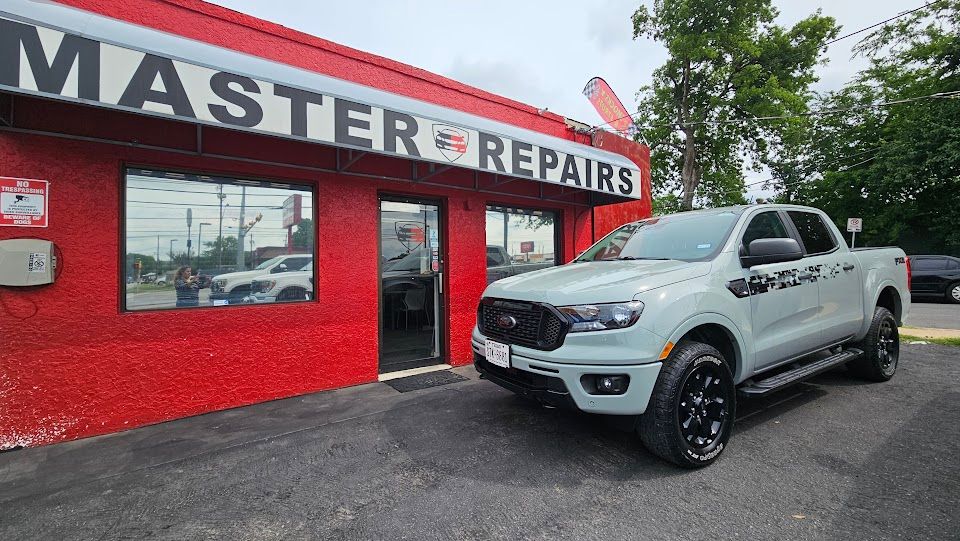 Gray Ford Ranger pickup truck parked in front of a red auto repair shop with the sign 
