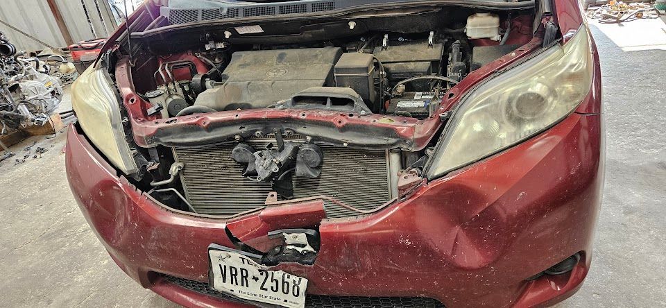Red minivan with front-end damage; hood open, engine visible; Texas license plate; garage setting.