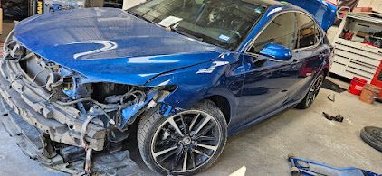 A blue car with extensive front-end damage. It is missing a bumper and other parts.