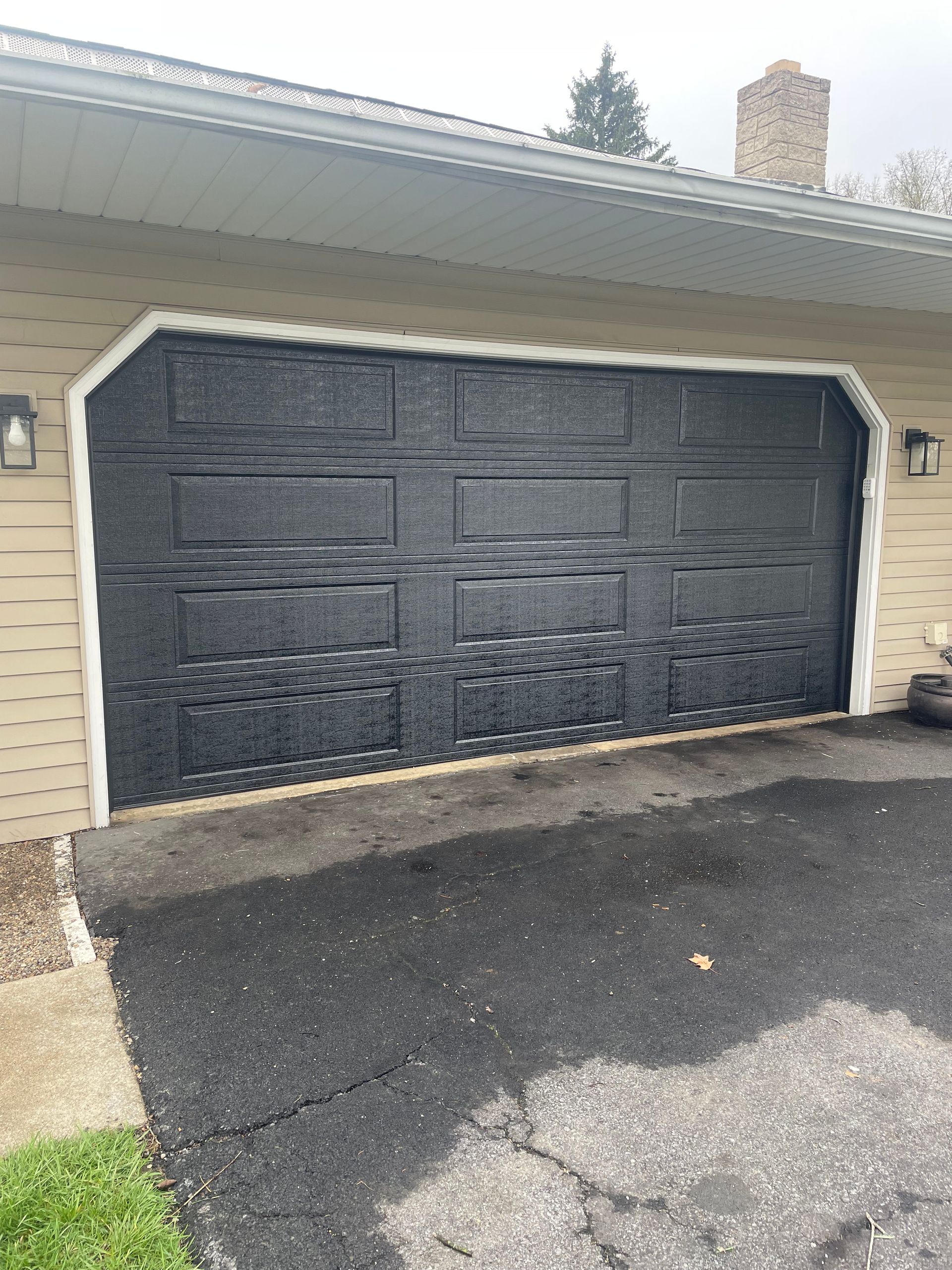 Black garage door on beige house with white trim and asphalt driveway