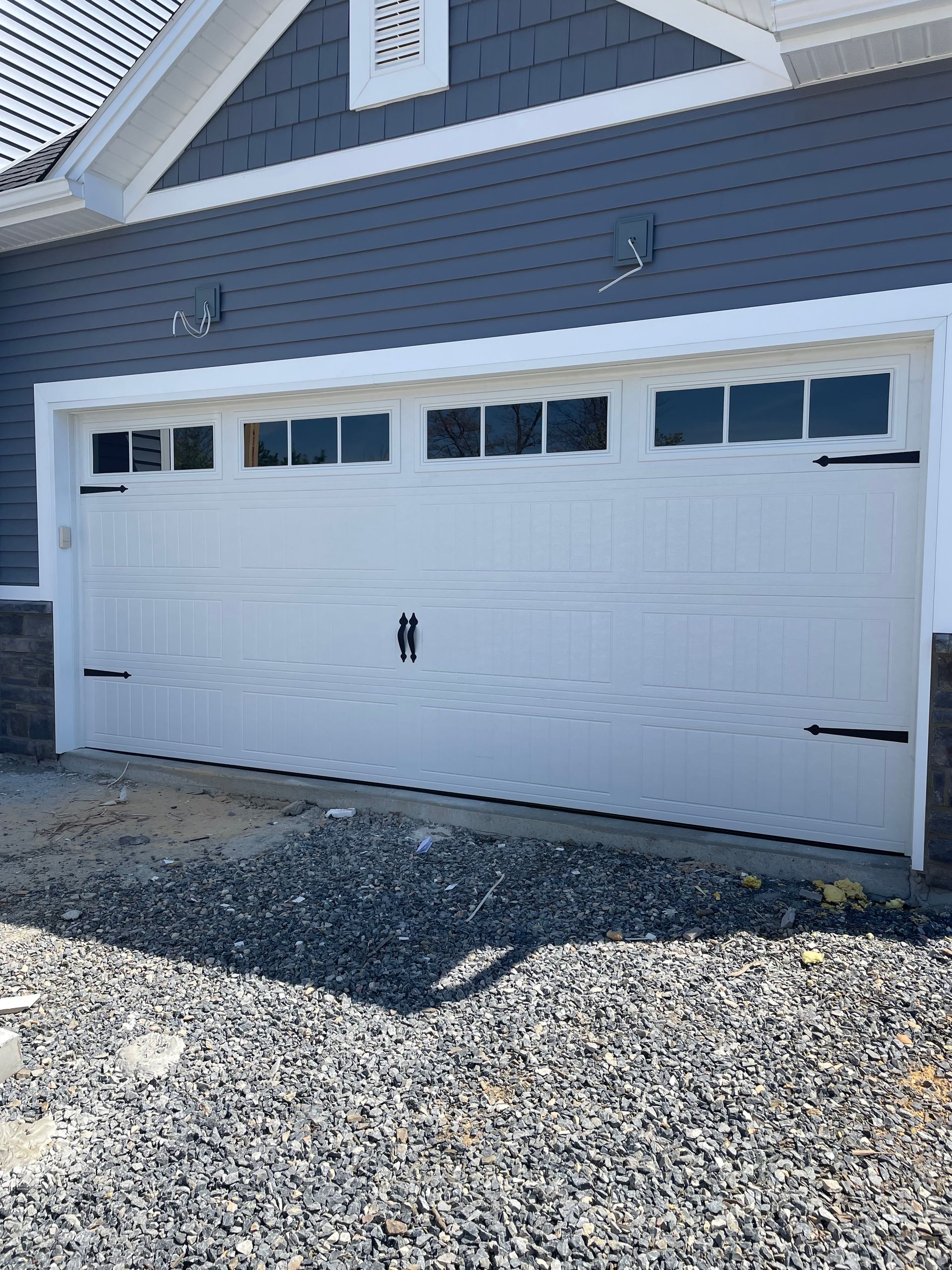 White double garage door on a gray house with blue siding and a gravel driveway