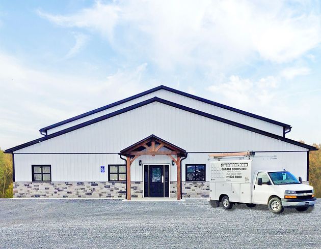 A white metal warehouse-style building with a stone-accented entrance and a parked white utility truck on a gravel lot.