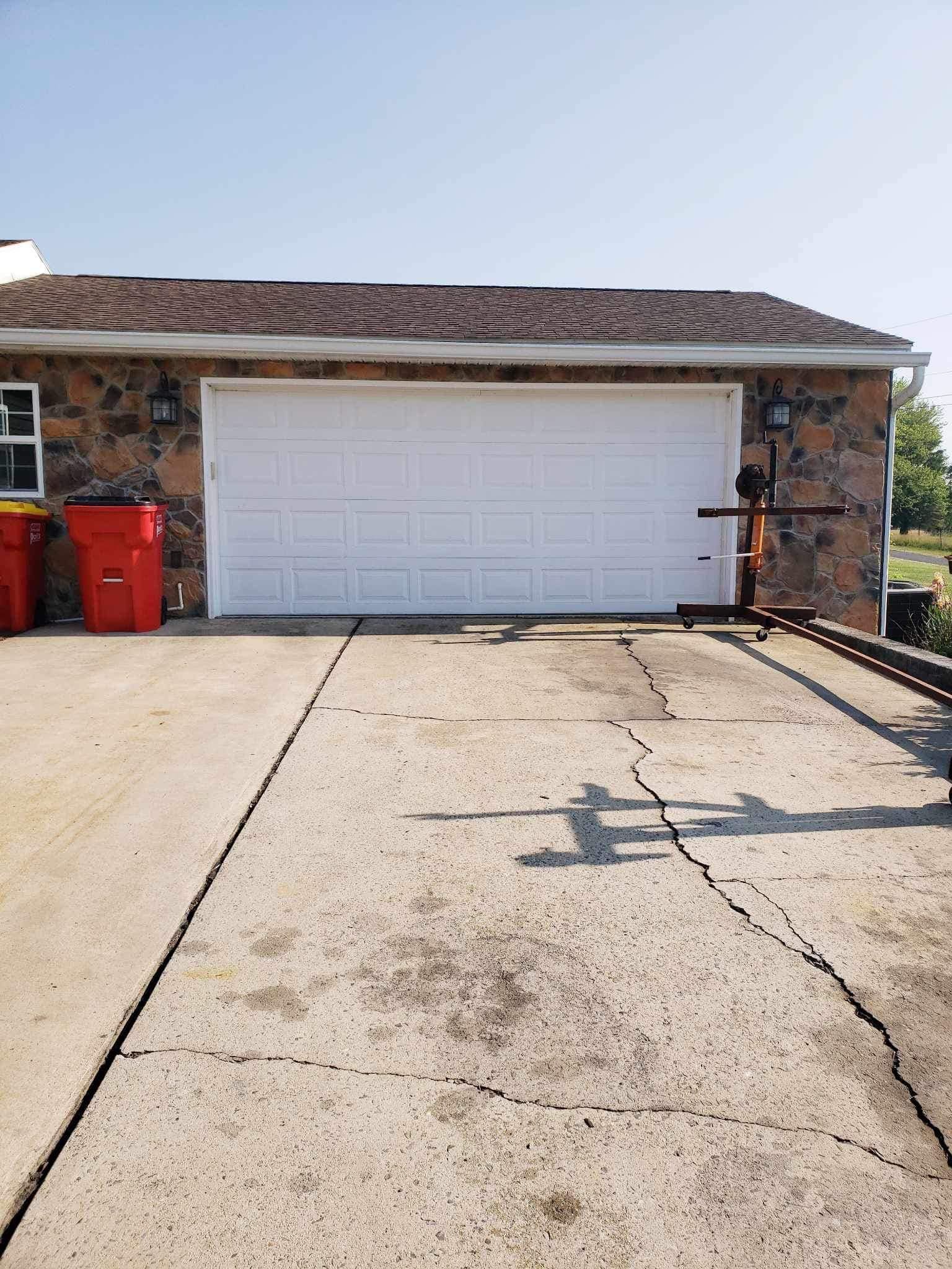 A single-story building with stone-textured walls and a white garage door, featuring a cracked concrete driveway in front.