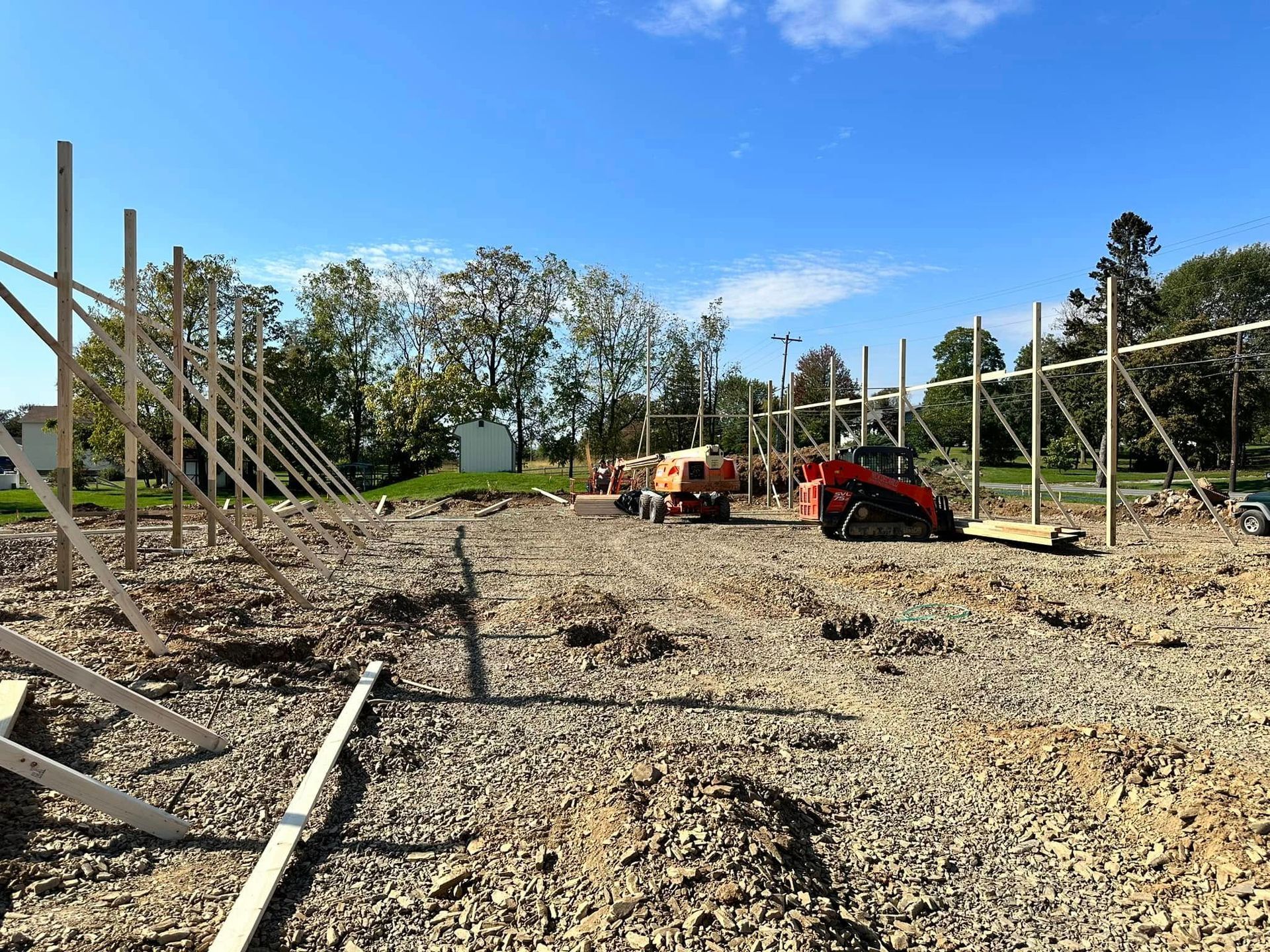 Construction site with vertical wood beams, gravel ground, and heavy machinery under a clear blue sky.