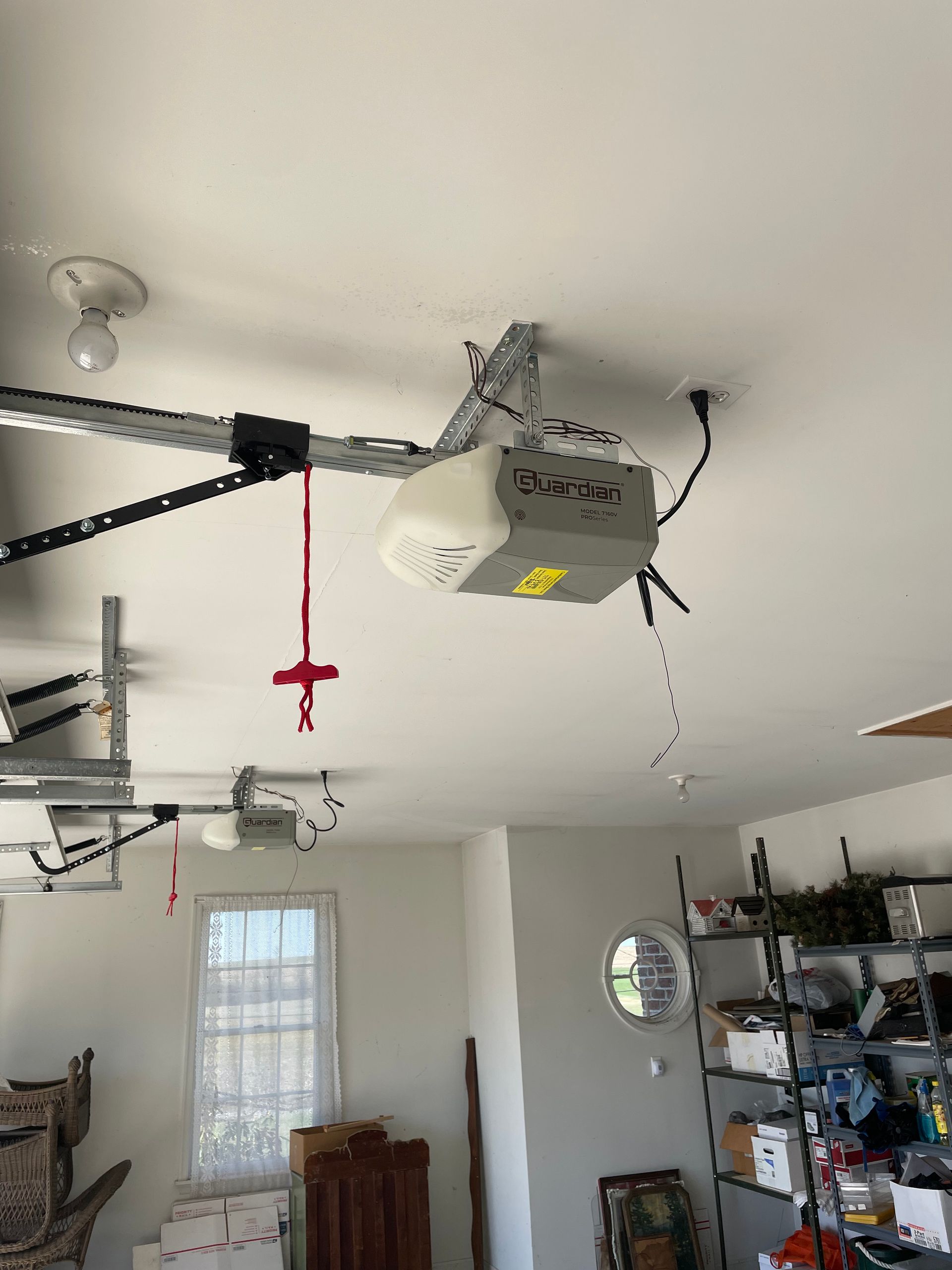 A gray garage door opener motor mounted to the ceiling with a red emergency release handle hanging down.