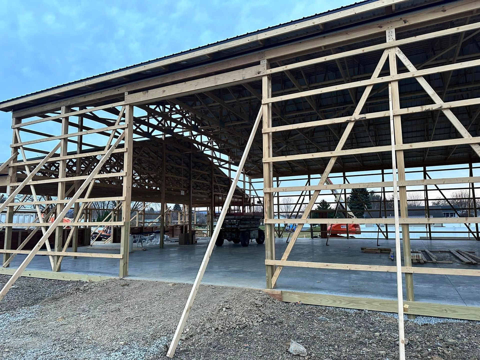 Construction site of a large wooden post-frame building structure with a concrete floor under a cloudy sky.