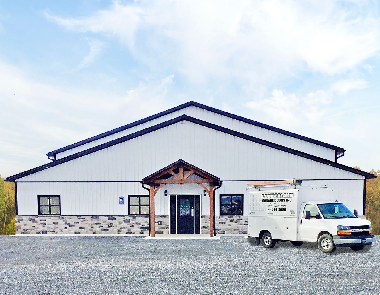 A white industrial building with a stone-accented entryway and a utility truck parked in front on a gravel lot.