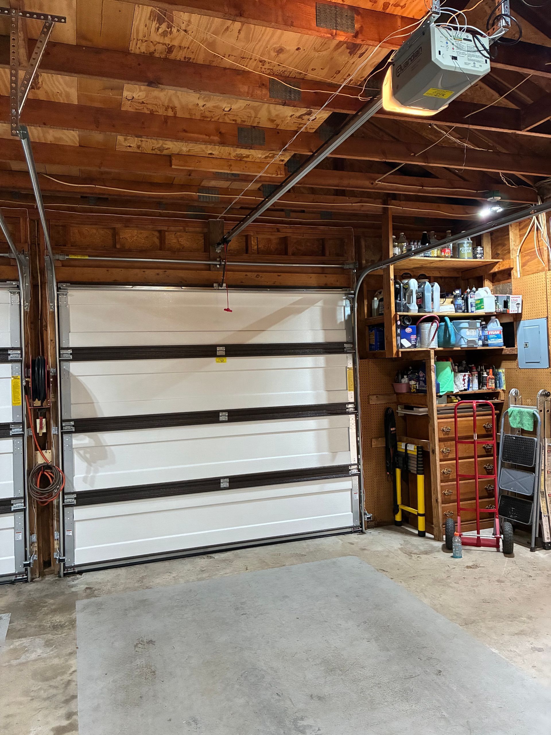 Interior of a garage with a closed white door, exposed wooden ceiling, and shelving on the right.