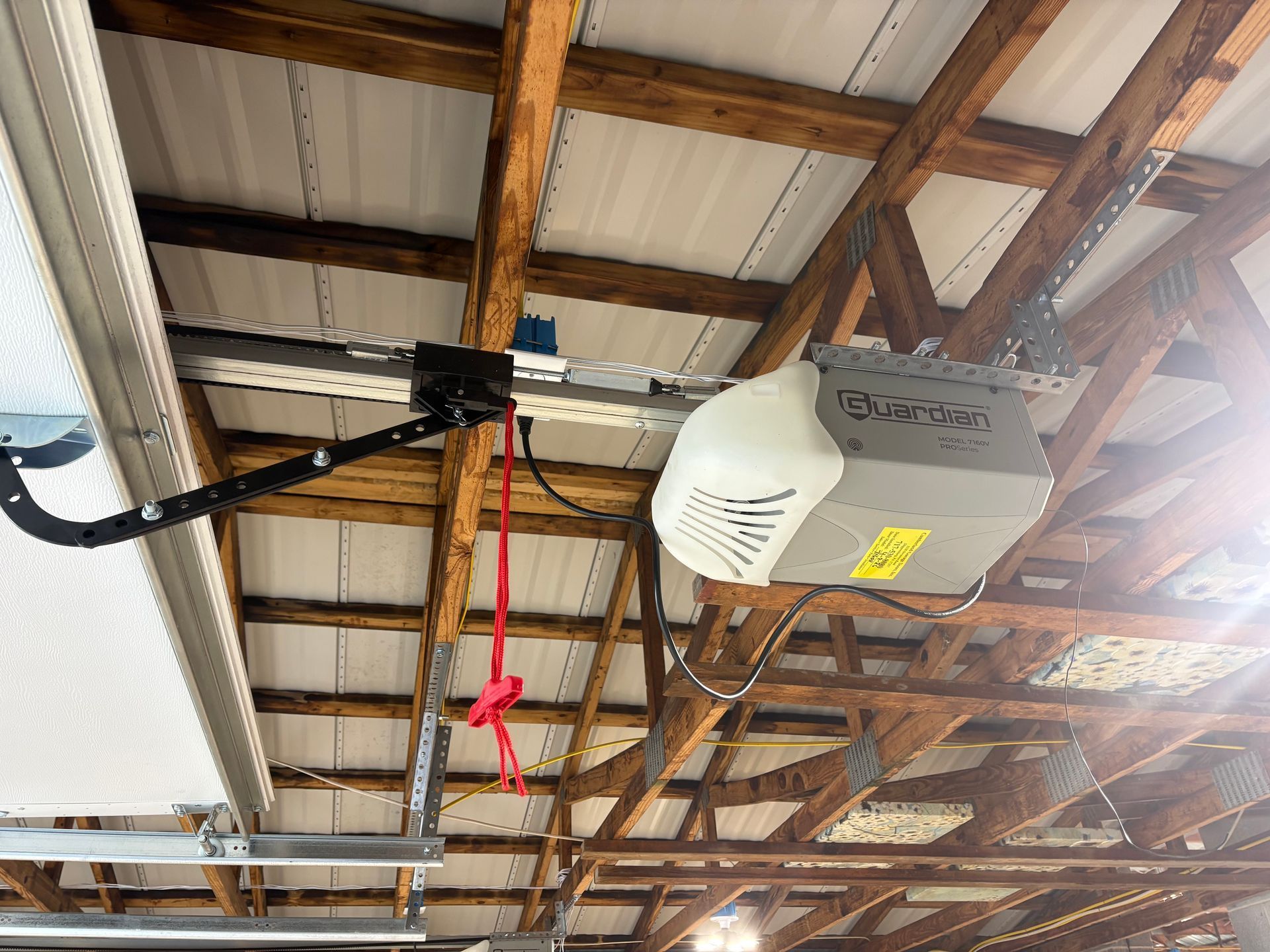 Garage ceiling with overhead door opener, wooden beams, and hanging red strap near exposed rafters