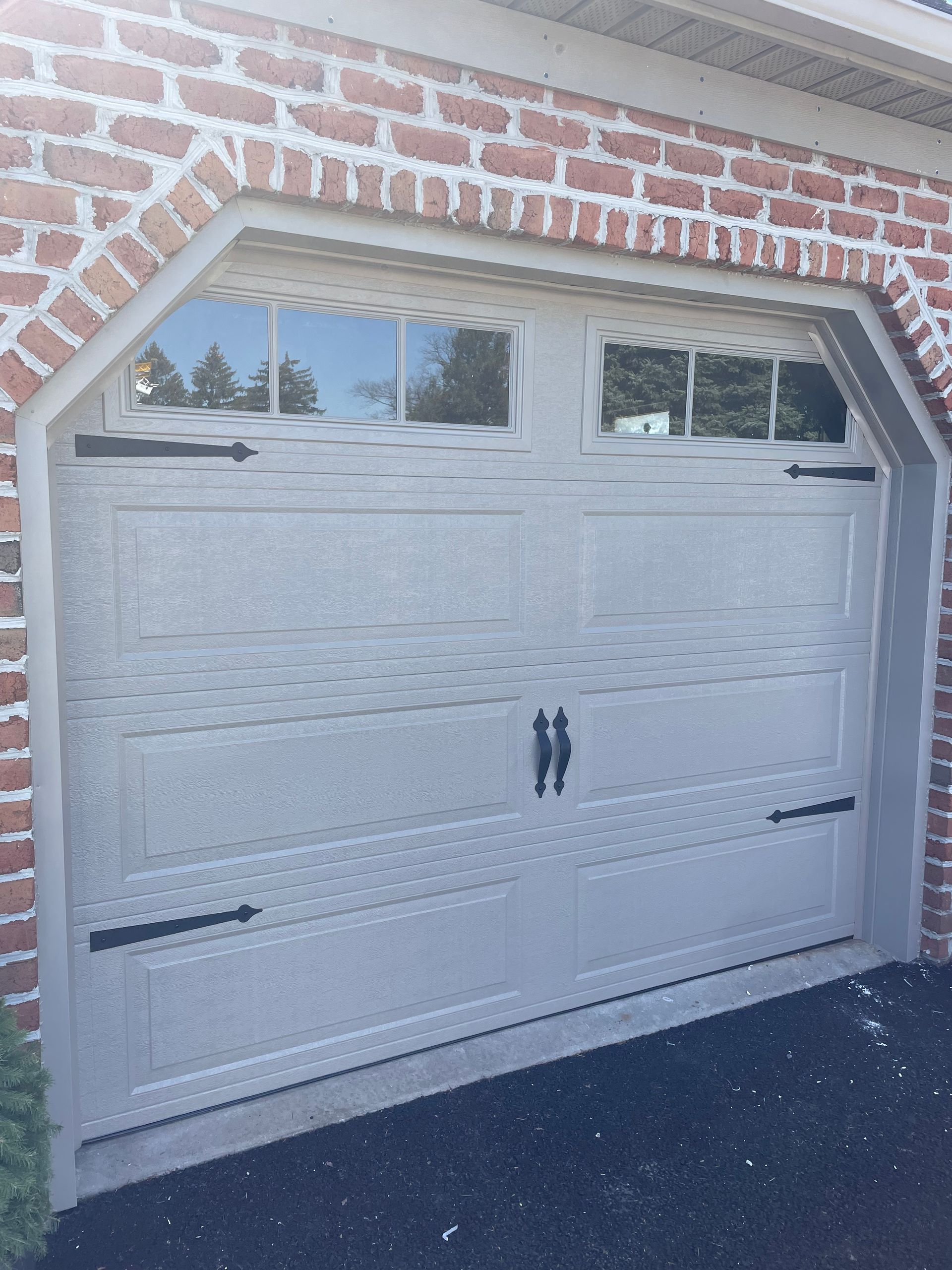 A light-colored residential garage door with rectangular panels, top window inserts, and decorative black hardware.