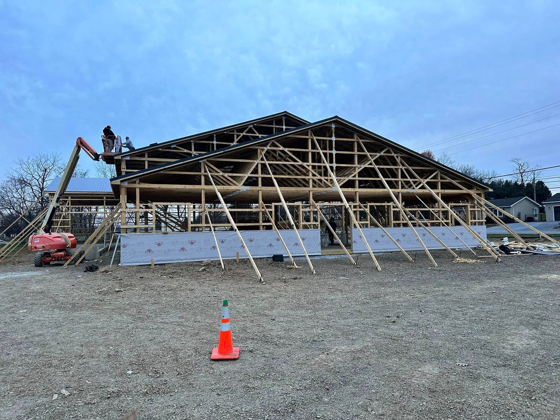 Construction workers on a lift frame the roof of a wooden building under construction against a twilight sky.