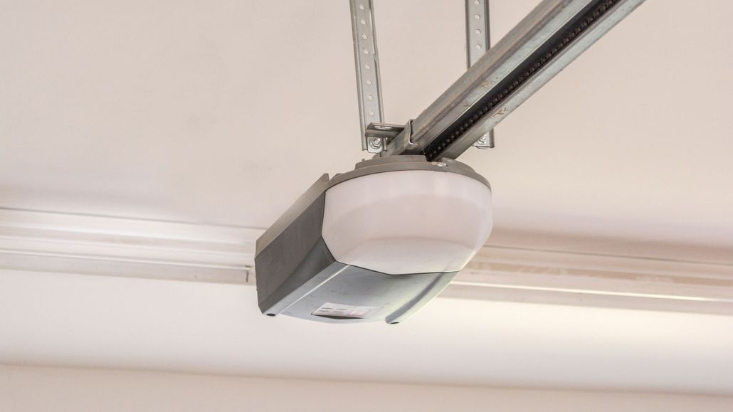 A white and grey garage door opener mounted to a ceiling with a metal support bracket.
