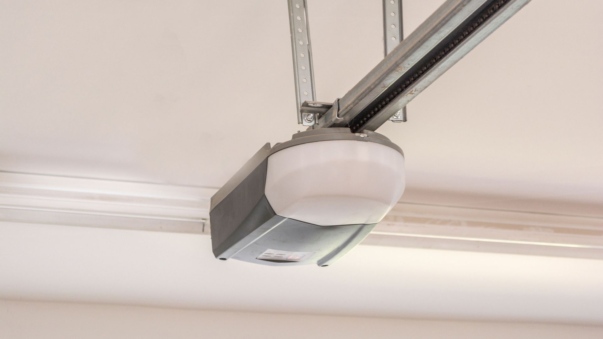 A white and grey garage door opener mounted to a ceiling with a metal support bracket.