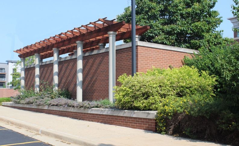 A brick wall with a wooden pergola on top of it