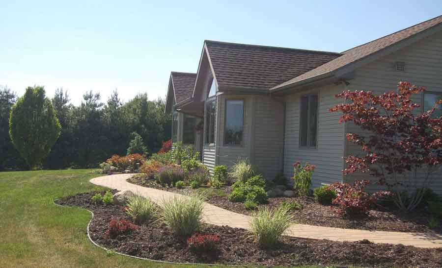 A house with a walkway leading to it and a lush green yard.